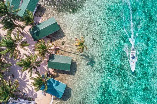 Aerial drone view of Tobacco Caye small Caribbean island with palm trees and bungalows in the Belize Barrier Reef