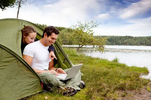 A couple looking at a computer while camping in a tent