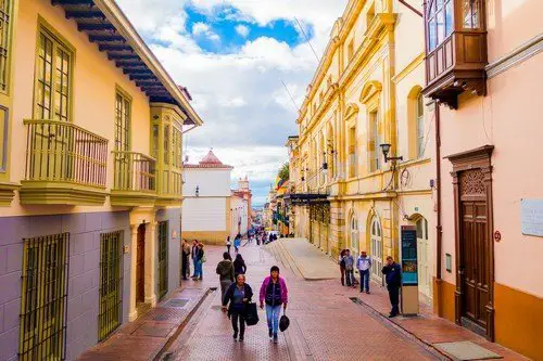 Typical charming street in old part of Bogota with people walking on red stoned pavements sorrounded by spanish colonial architecture and yellow buildings - ultimate colombia travel guide