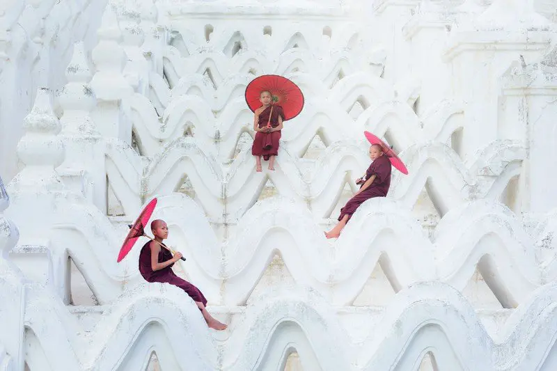 Unidentified Asian young monk holding red umbrellas on the Mya Thein Tan Pagoda at Mingun, Mandalay Myanmar. budget myanmar travel guide