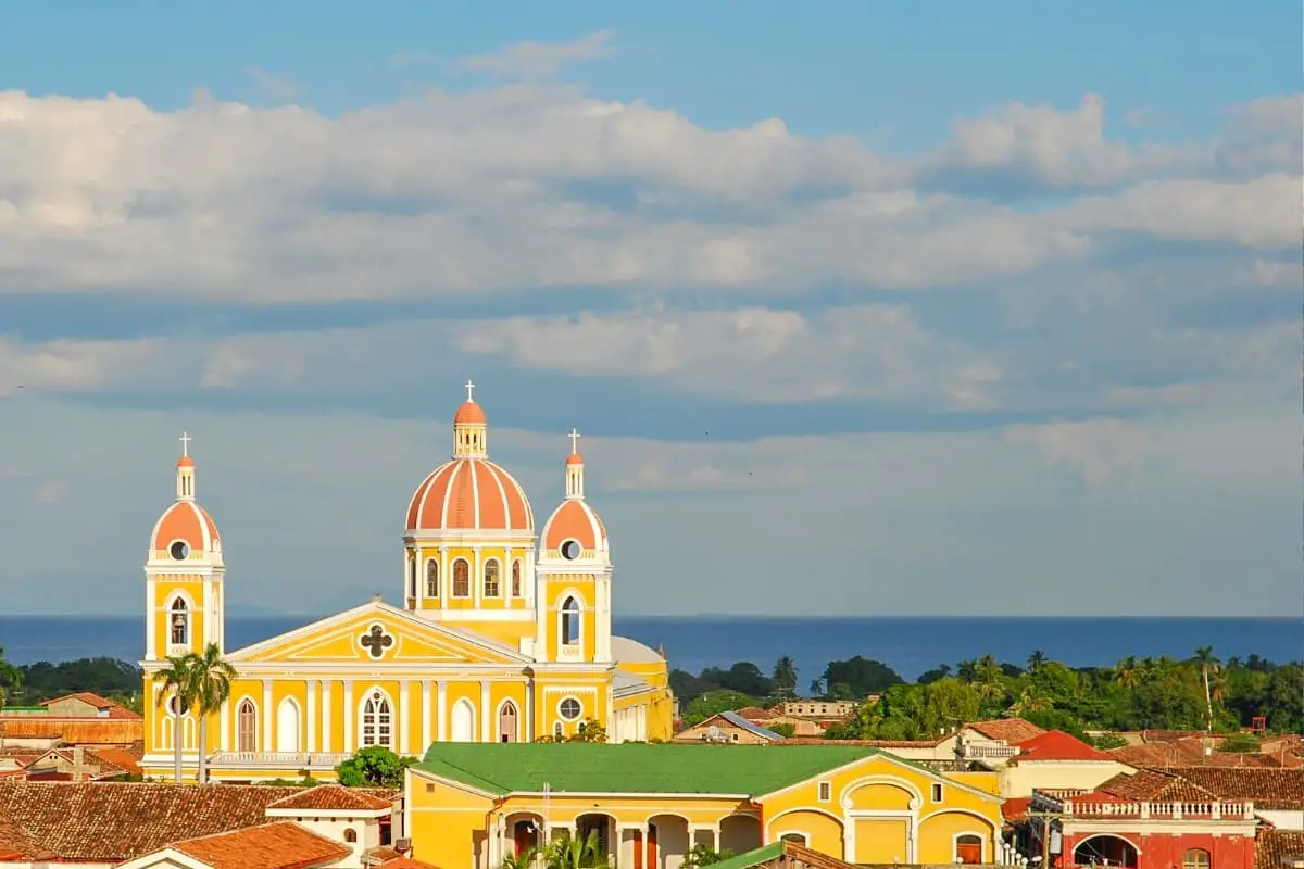 The skyline of Granada, Nicaragua, with its yellow cathedral, rooftops in Spanish-colonial-style architecture and Lake Nicaragua in the background.