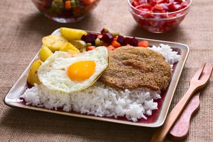 Traditional Bolivian Dish Called Silpancho. It begins with a bed of rice and is topped with a pan-fried burger, salsa, fried potatoes, and an over easy egg - Authentic Argentina Food Recipes for Dinner